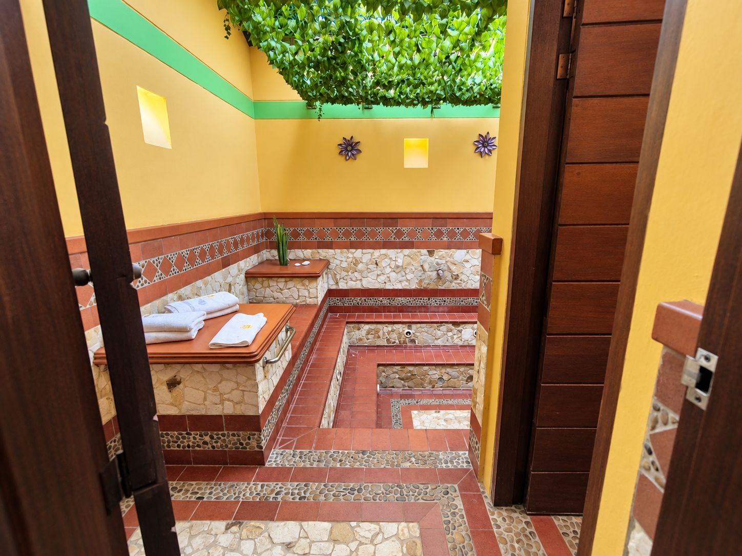 A bathroom with a stone and tile floor, a bench, and a green plant overhead.