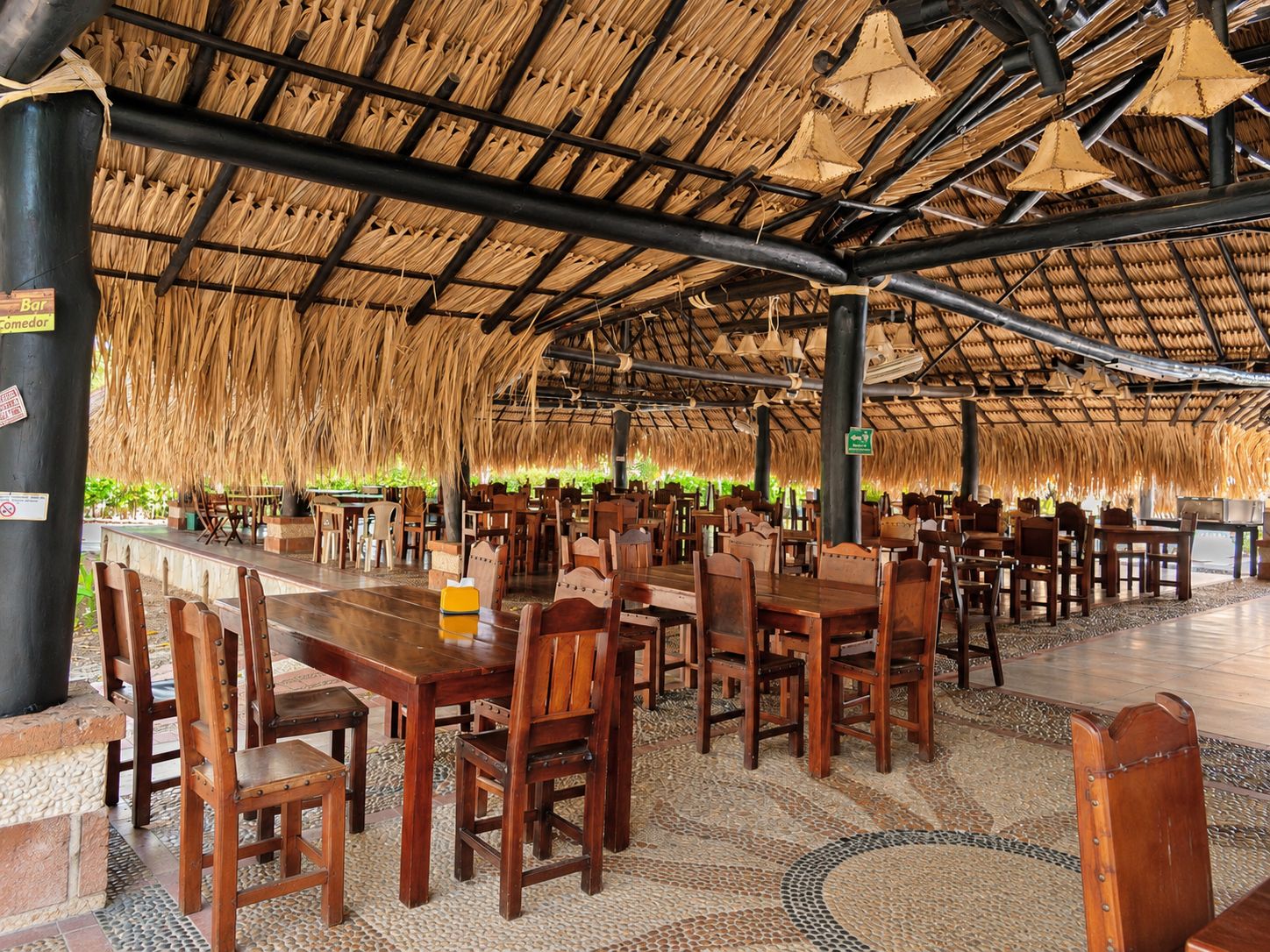 An indoor dining area with thatched ceilings, wooden tables, and chairs.