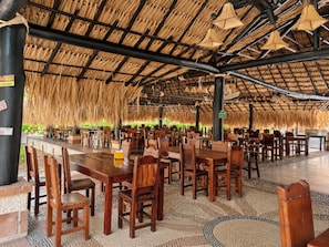 Un comedor interior con techos de paja, mesas y sillas de madera.