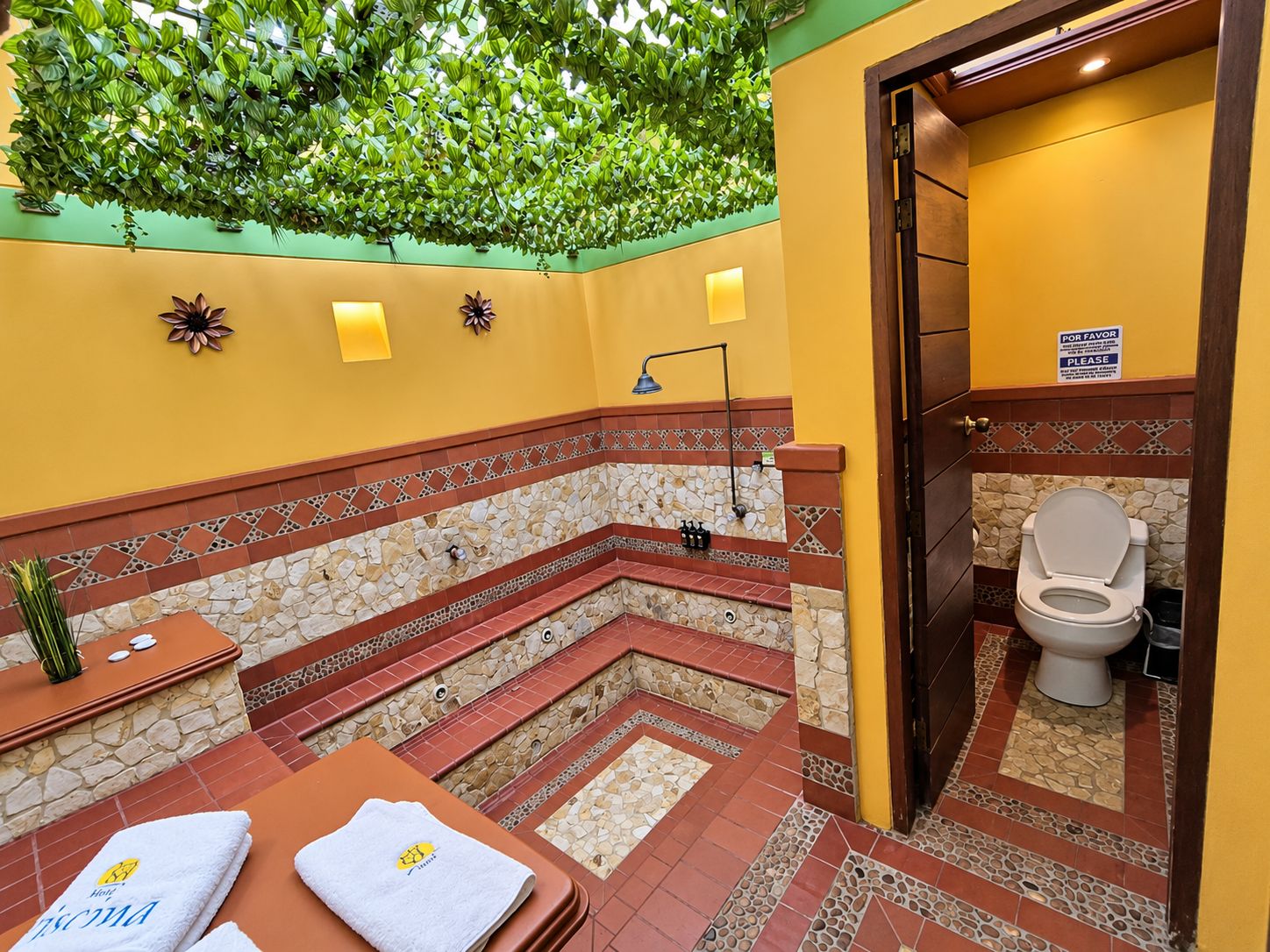 Une salle de bain avec un mur décoré d’une mosaïque en pierre, un espace douche et des toilettes.