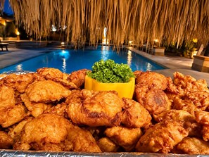 Zona de piscina con una mesa de pollo frito y un bol amarillo de guarnición verde.