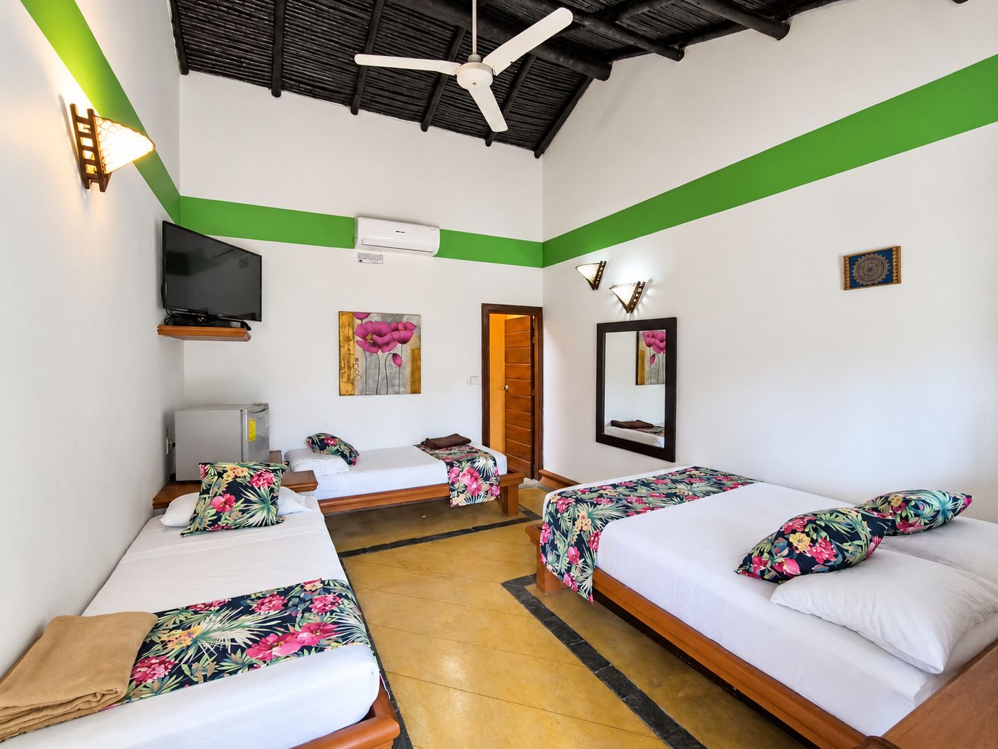 A hotel room with two beds, a ceiling fan, a flat-screen TV, and a painting on the wall.