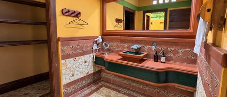 Un baño con piso de baldosas de piedra, tocador de madera con lavabo y espejo arriba.