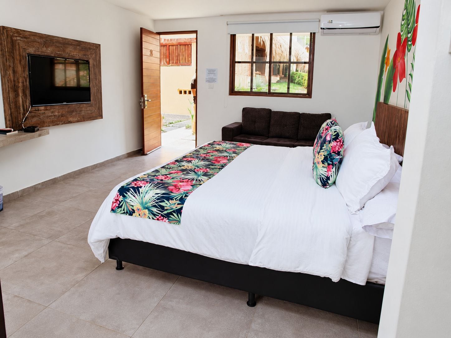Un dormitorio con cama, televisor montado en la pared, ventana con vistas y aire acondicionado.