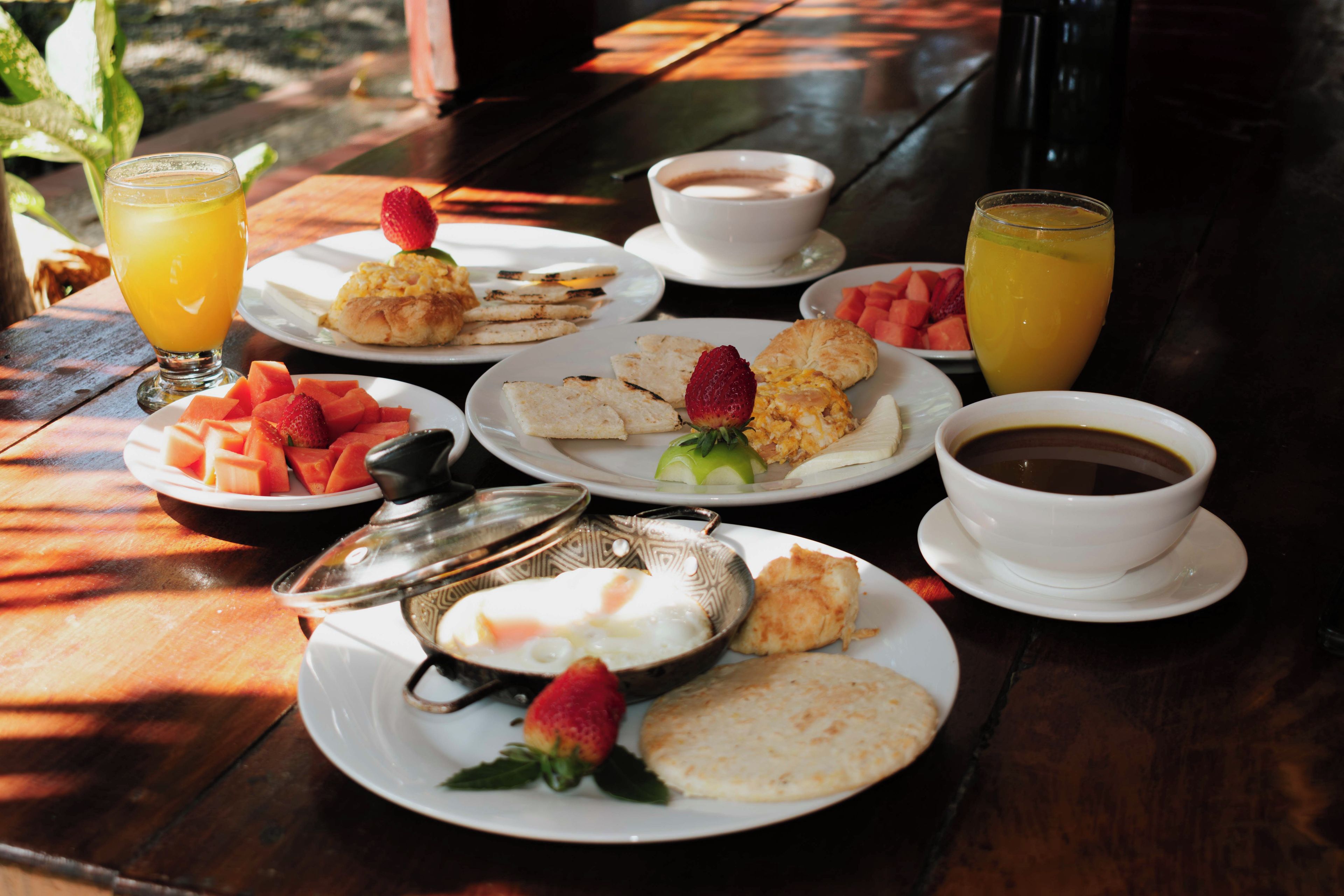 Una mesa servida con alimentos para el desayuno, incluyendo tostadas, fruta y bebidas.