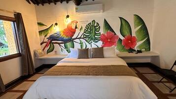 Une chambre avec un grand lit, une fenêtre avec des rideaux, une fresque murale représentant un perroquet et des feuilles tropicales, et un banc avec un coussin.