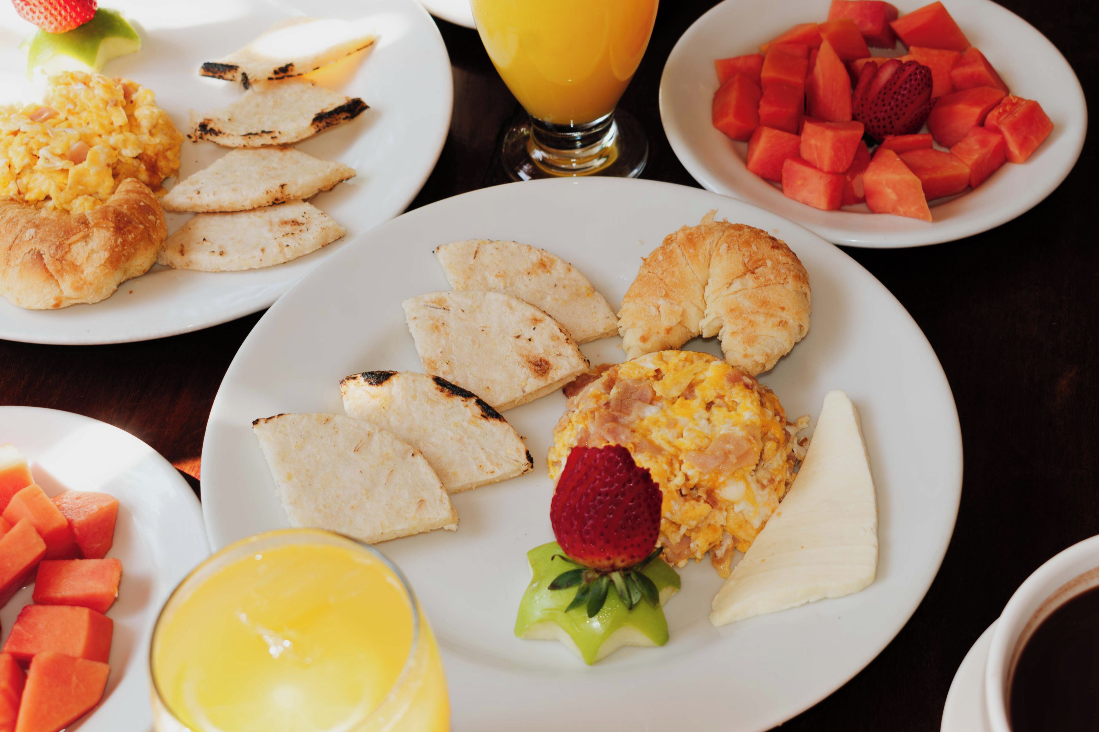 Un desayuno con platos de huevos revueltos, tostadas y fruta.