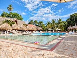 Un área de piscina con sillones de descanso y sombrillas de paja.
