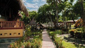 A tropical resort with a thatched-roof structure, a paved pathway, and lush greenery. - Hotel Porton del Sol  (Santa Fe de Antioquia)