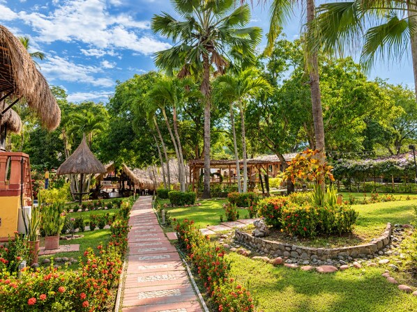 A tropical resort with a paved pathway, palm trees, and thatched-roof structures.