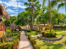 Un resort tropical con un camino pavimentado, palmeras y estructuras de techo de paja.