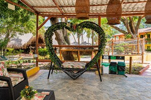 An outdoor seating area with a heart-shaped planter, wicker furniture, and a covered pergola with hanging lights. - Hotel Porton del Sol  (Santa Fe de Antioquia)