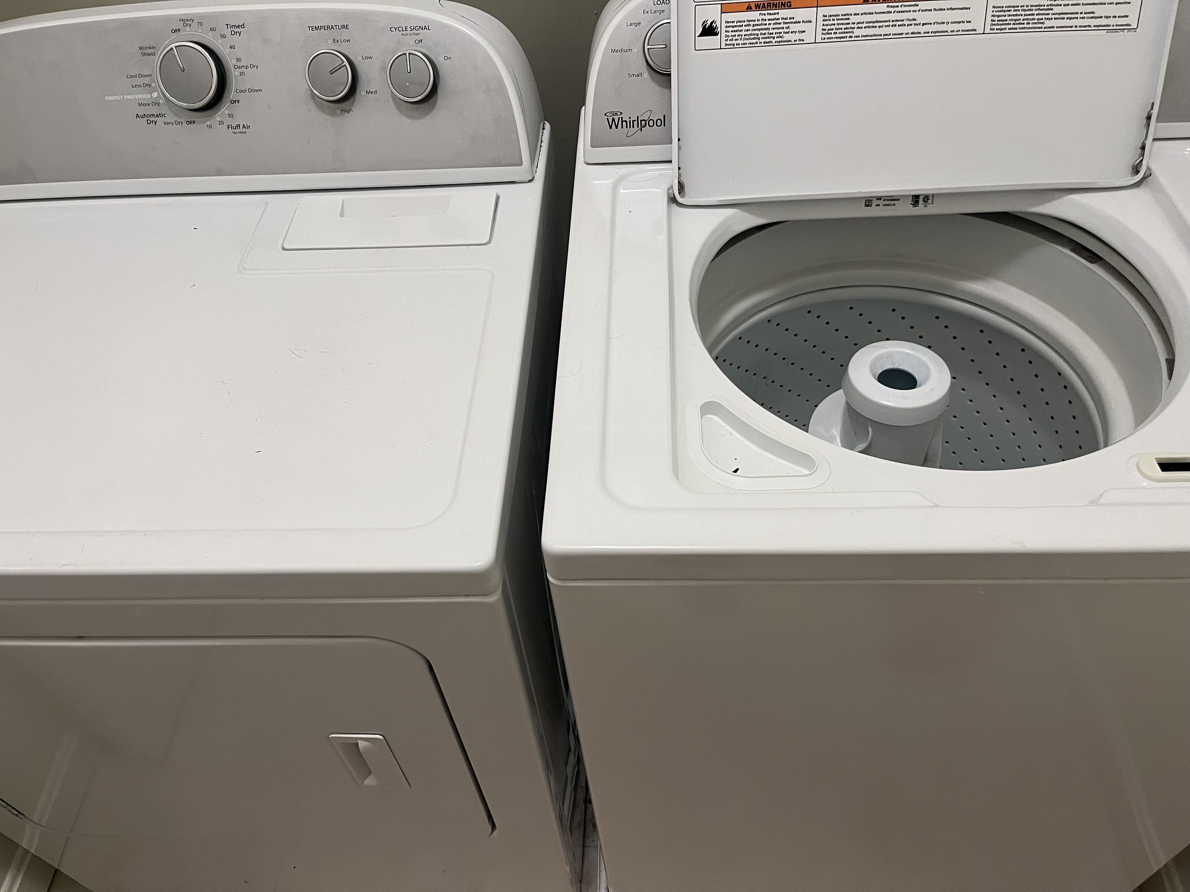 A front view of a front-loading washer and dryer unit with control knobs and a warning label.