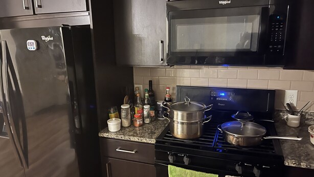 A kitchen with a refrigerator, microwave, stove, and various kitchen items on the counter.