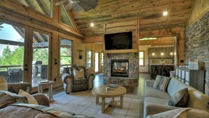 A spacious living room with a stone fireplace, comfortable seating, and a large TV. - 4 BR w Views, Private trails, hot tub, 3 king beds, EV Charger (Mineral Bluff)
