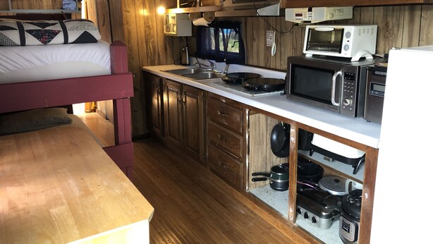 A compact kitchen with wooden cabinets, a microwave, a stove, and a sink. - Antique1958Spartan CamperOceanLakes Cmpgrnd, I-33.Golf Cart for July,Aug rentals (Myrtle Beach)