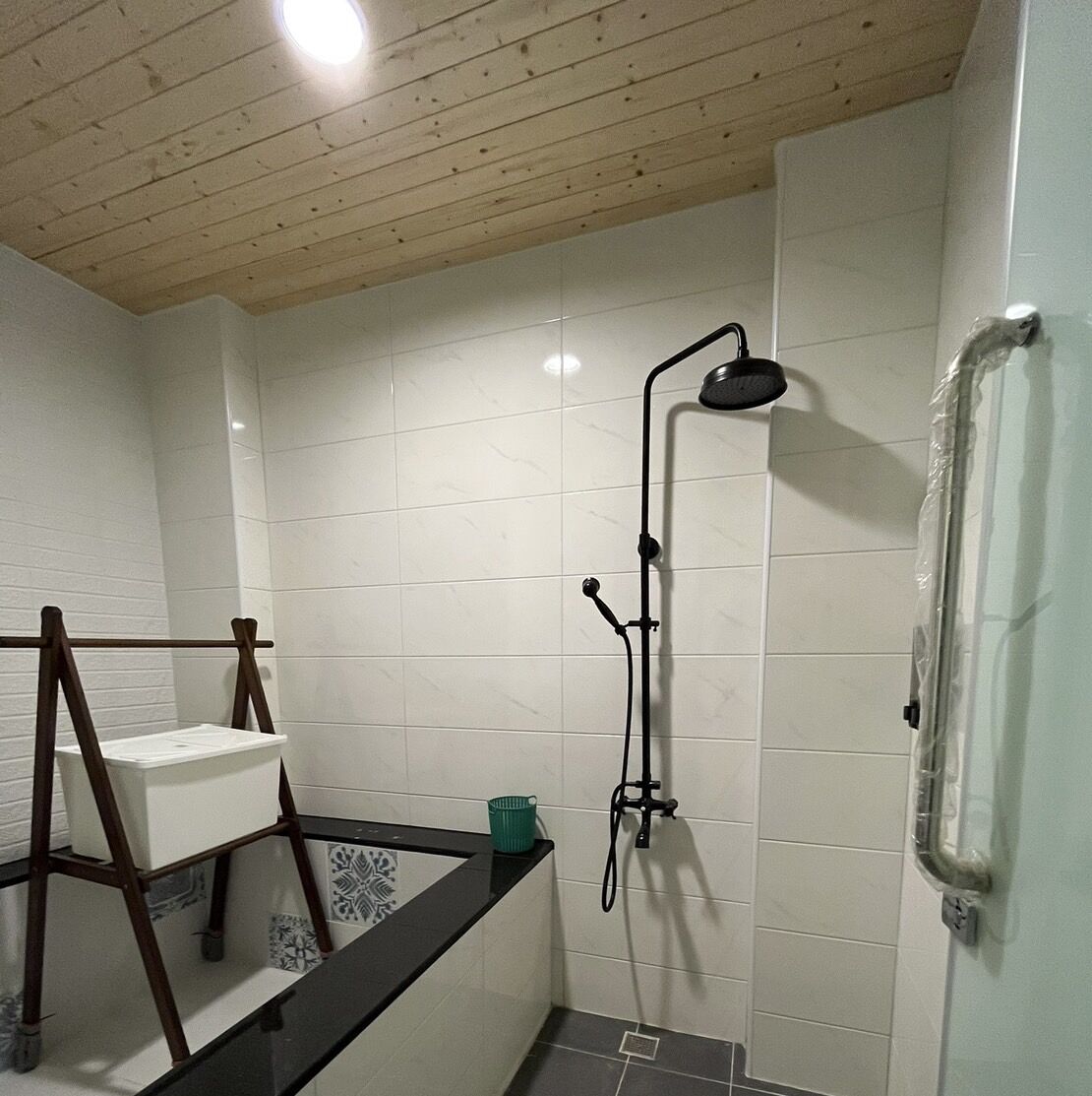 A bathroom with a shower, a wooden ceiling, and a tiled wall.