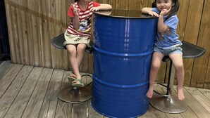 Two children sitting on stools at a blue barrel. - A BA LI BI Duck (Tainan)