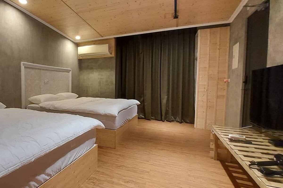A hotel room with two single beds, a wooden floor, a television, and a curtain.