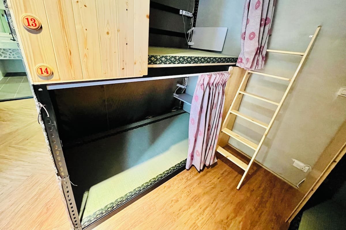 A compact room with a bunk bed, a small desk with a laptop, and a curtain.