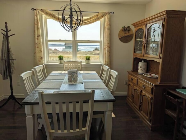 A dining area with a table and chairs, a chandelier, a window with curtains, a coat rack, and a wooden cabinet.