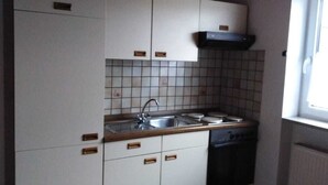 Una cocina compacta con alacenas blancas, salpicadero de azulejos, un lavamanos, estufa y ventanal.