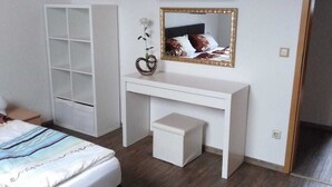 Un dormitorio con una cama, un escritorio blanco con un espejo, un taburete blanco pequeño y un armario blanco.