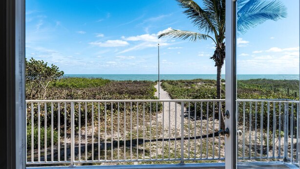 A balcony with a view of a beach, a palm tree, and a clear sky. - Private Beachfront House (Fort Pierce)