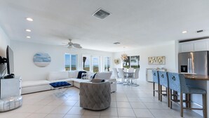 A modern living room with a white sofa, a grey ottoman, and a dining area with a white table and chairs. - Private Beachfront House (Fort Pierce)