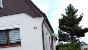 A house with a white exterior, number 26, a stone staircase leading to the front door, and a small garden with plants and a tree. - FEWO in ruhiger Lage (Niedersachsen - Buxtehude)