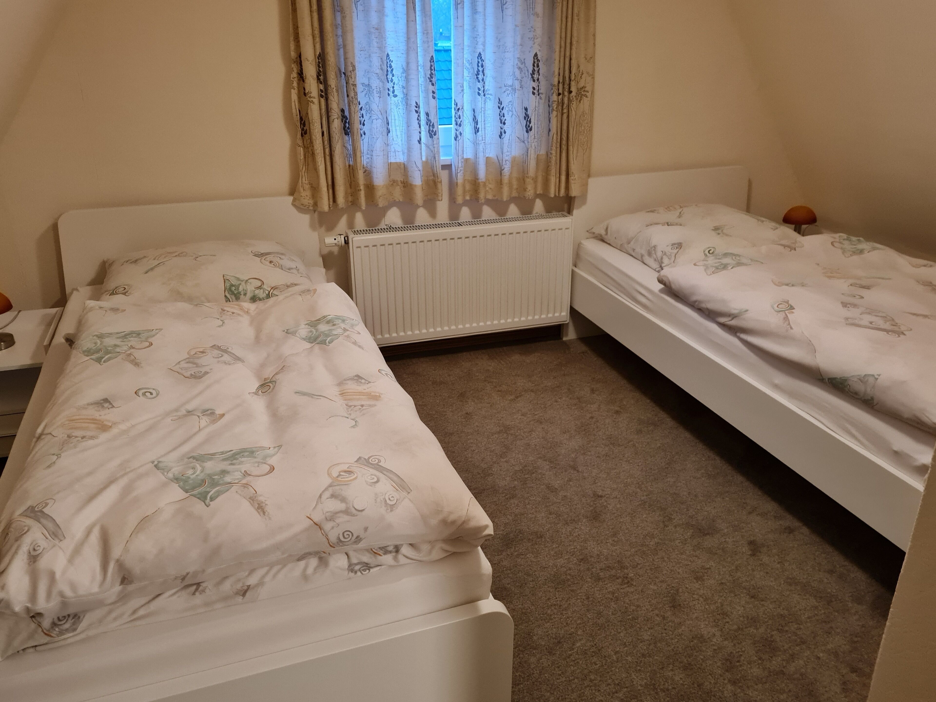 A bedroom with two single beds, a radiator, and a window with curtains.