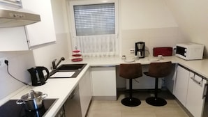 A compact kitchen with a stove, sink, and two stools. - FEWO in ruhiger Lage (Niedersachsen - Buxtehude)