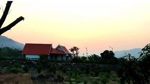 A house with a red roof and white walls, surrounded by greenery and a stone wall. - Valley Villa with Private Pool (Lonavala)