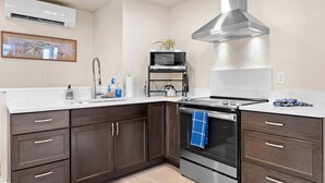 Une cuisine moderne avec des meubles de couleur bois foncé, une hotte de cuisine en acier inoxydable, un four à micro-ondes et une bouilloire posés sur le plan de travail.