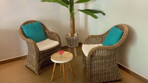 Habitación de esquina con dos sillones de mimbre, una mesita redonda y una planta grande en maceta.