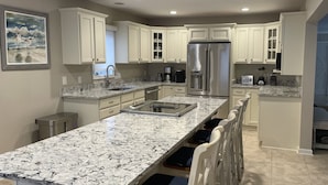A modern kitchen with white cabinetry, a large island with a marble countertop, and a stainless steel refrigerator. - 2 Spotted Sandpiper at The Sea Pines Resort (Hilton Head Island)