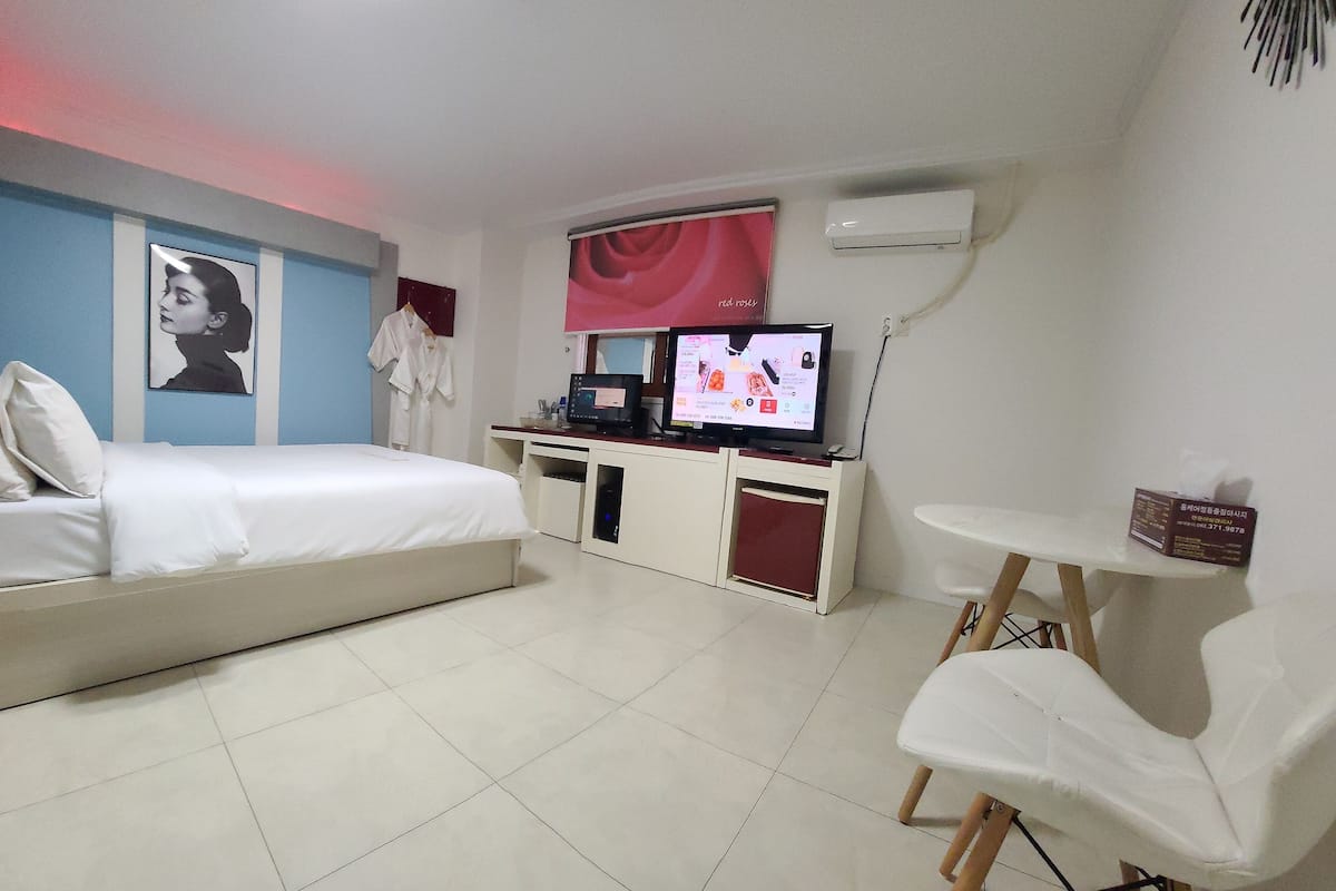 A hotel room with a bed, a desk with a computer, a TV, and a chair.