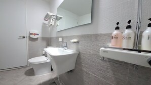 A modern bathroom with a white toilet, a freestanding bathtub, and a vanity with a mirror. There are two bottles of shampoo and body wash on the vanity. - Dream Motel (Gwangju)