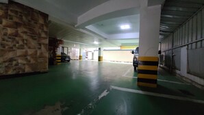 A parking garage with green flooring, yellow and black striped pillars, and a white car parked in the distance. - Dream Motel (Gwangju)
