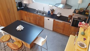A modern kitchen with wooden cabinets, a black countertop, stainless steel appliances, and a central island with chairs. - Very pleasant family home in Saint-Enogat Dinard (Dinard)