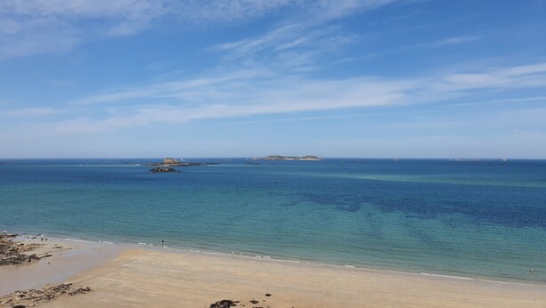 A beach with clear blue water, a sandy shore, and a distant island with a lighthouse. - Very pleasant family home in Saint-Enogat Dinard (Dinard)