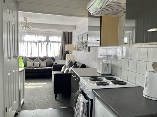 A modern kitchen with a built-in stove, a dining area with a table and chairs, and a living room with a sofa and a view of the outdoors.