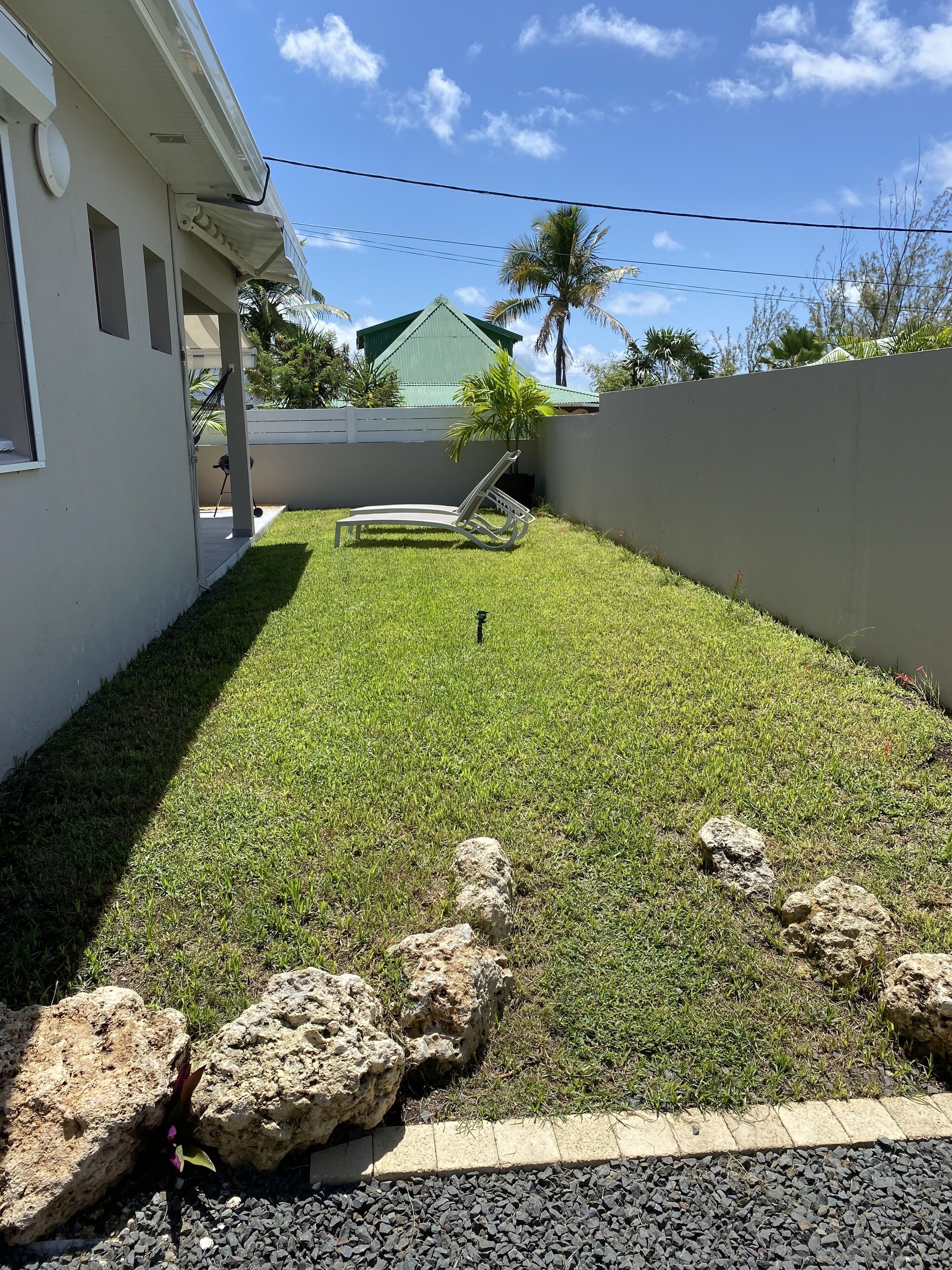 Un prato curato con una sedia a sdraio, un piccolo giardino roccioso e una casa sullo sfondo con tetto verde.