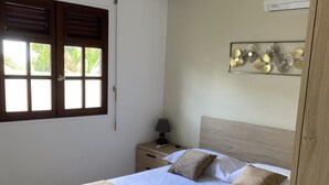 Un lit bien fait, avec une tête de lit en bois, une table de chevet avec une lampe et une fenêtre équipée de stores.
