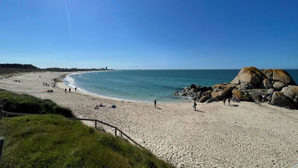 A beach with clear skies, calm waters, and rocky formations.