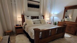 A bedroom with a wooden bed, two bedside tables, a nightstand, a mirror, and a large window with sheer curtains. - The Ritz serene spa sanctuary hot tub, mountain view, patio for the whole family (Las Cruces)