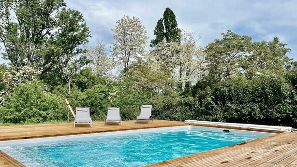 Piscina retangular com deck de madeira e três espreguiçadeiras brancas.