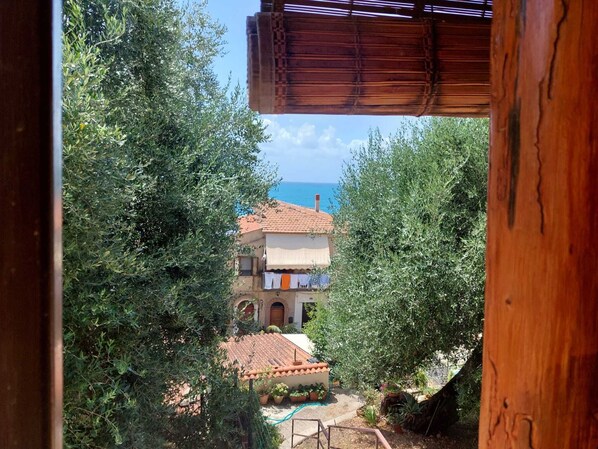 A villa with a tiled roof, surrounded by olive trees, and overlooking a body of water.