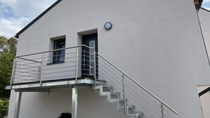Un edificio moderno con fachada blanca, un pequeño balcón con barandillas de metal y una puerta con un ventanal redondo.