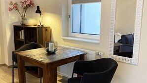 Una habitación acogedora con una mesa de madera, una silla negra, una estantería, un jarrón con flores, una lámpara y una ventana con vistas.